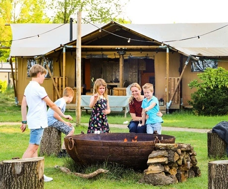 Camp fire with happy children in front of glamping tent.
